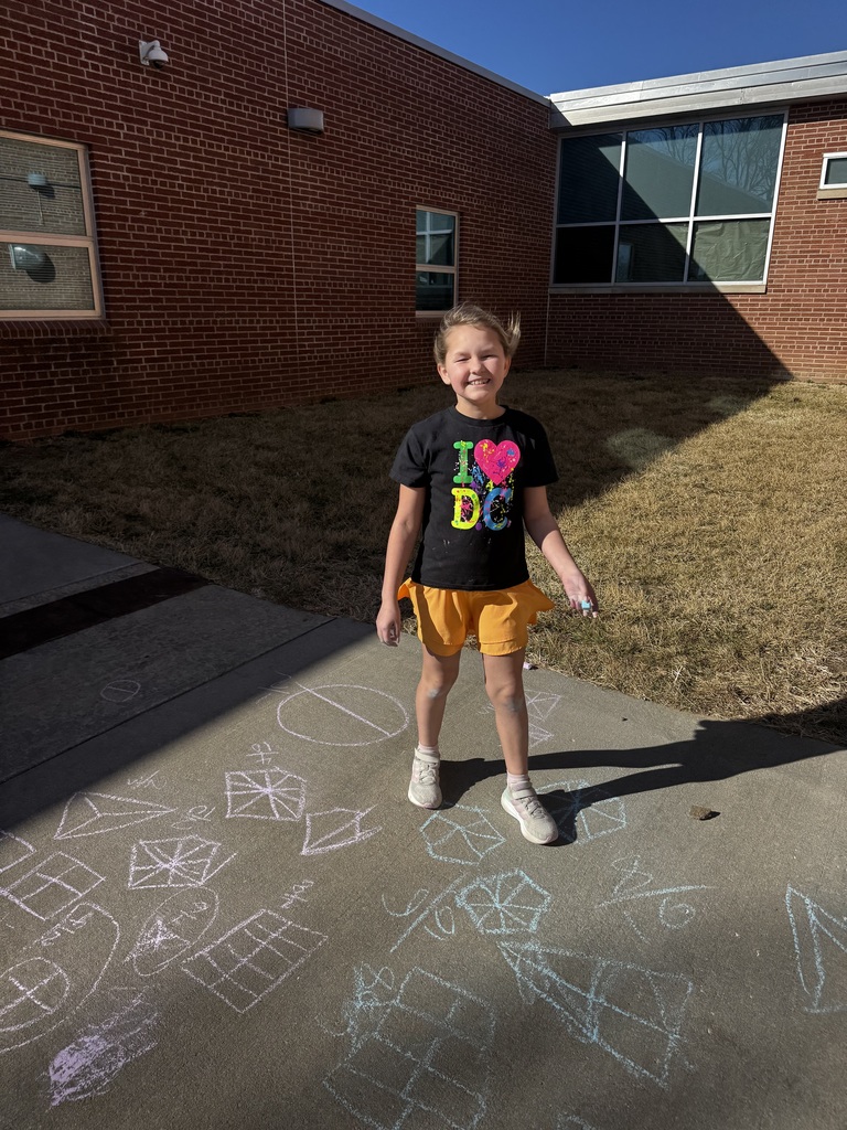 A girl stands on the ground smiling while chalk drawings show on the cement.