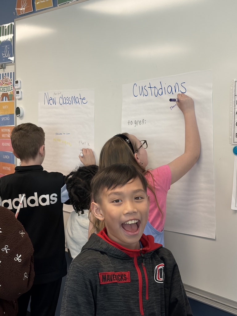 A student is smiling while classmates are writing on posters to a new classmate and our custodian with encouraging words. 