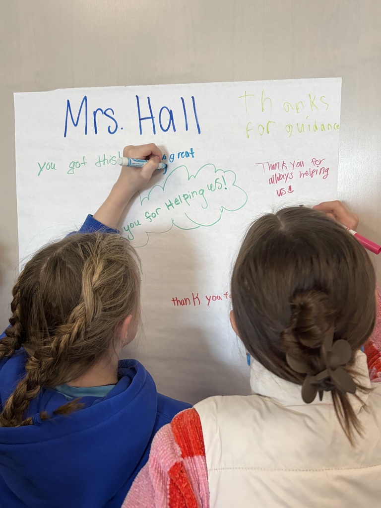 Two students are writing encouraging words on a poster for our counselor, Mrs. Hall.