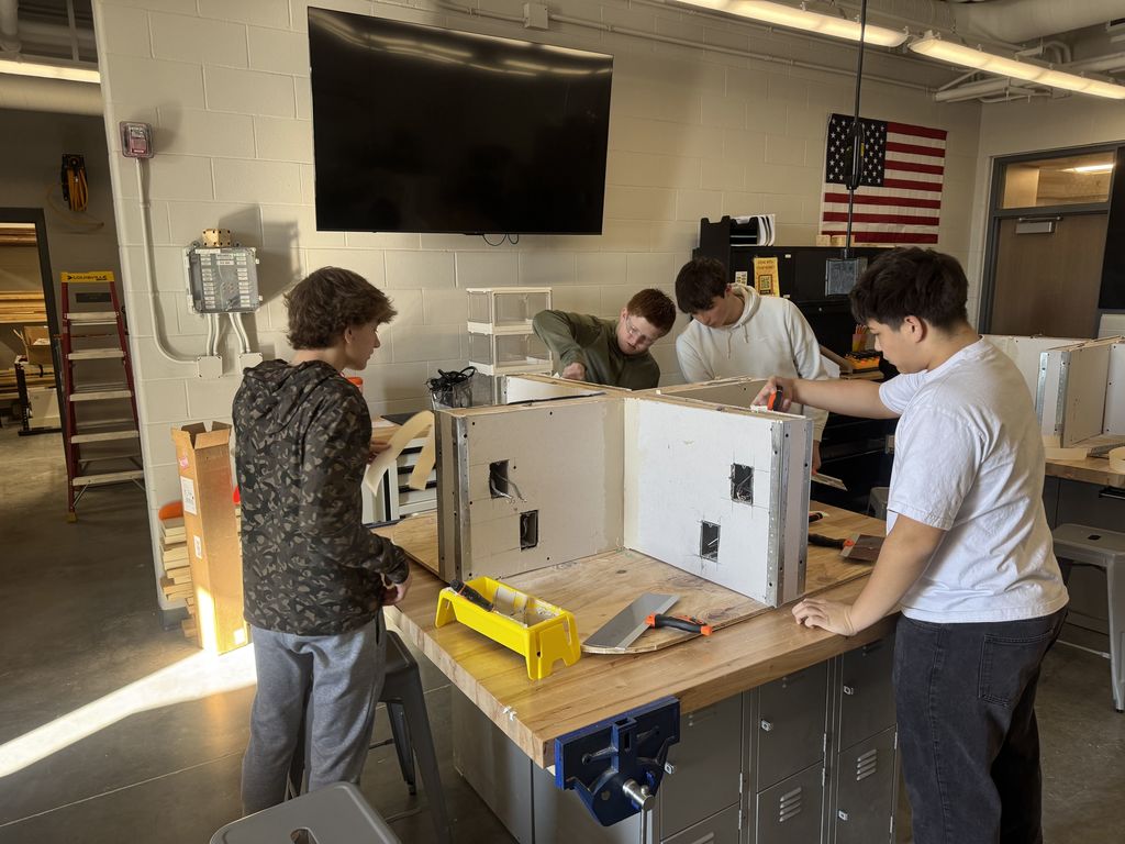 Four students stand around a table working on a drywall project. 