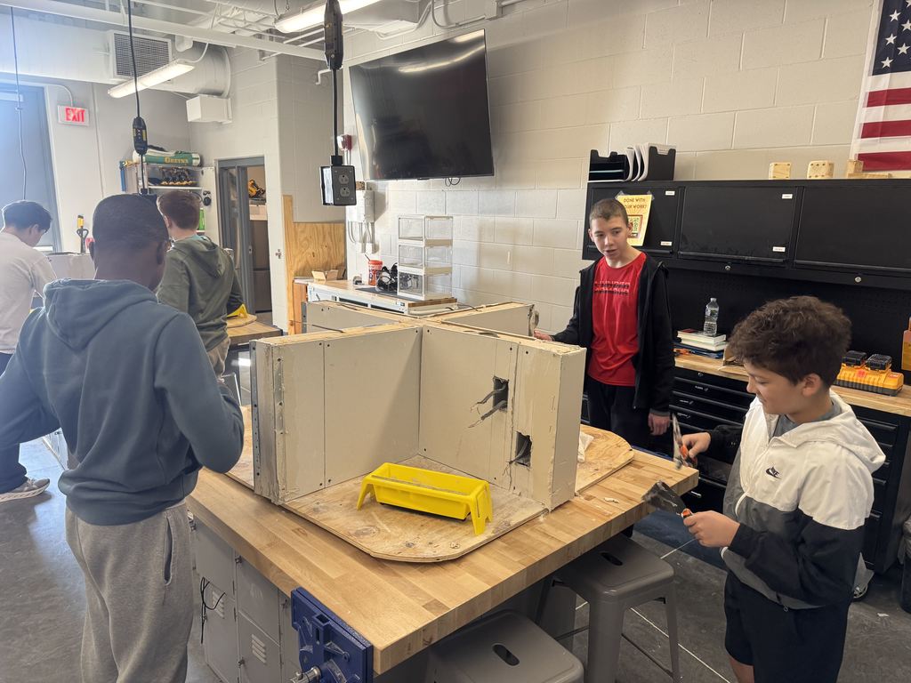 Four students stand around a table working on a drywall project. 