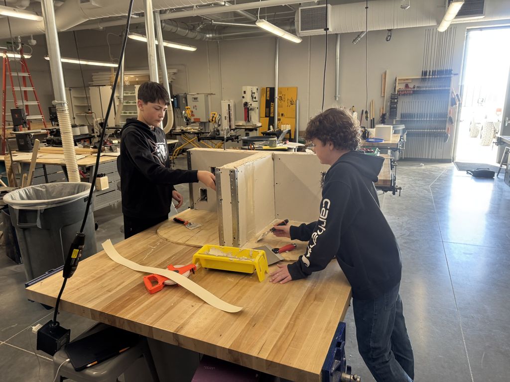 Two students are working at a table on a drywall project. 
