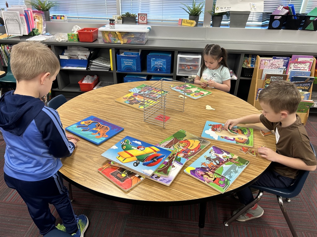 Three children sitting at a round wooden table in a classroom, focused on completing various wooden puzzles.