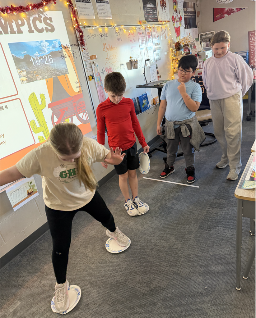 students 'skating' on paper plates in a classroom