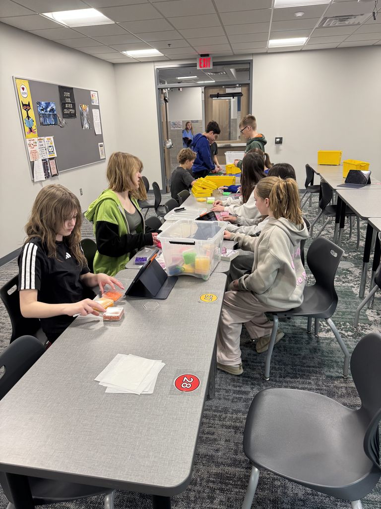 Students are sitting at a long table with Legos and Perler Beads. 