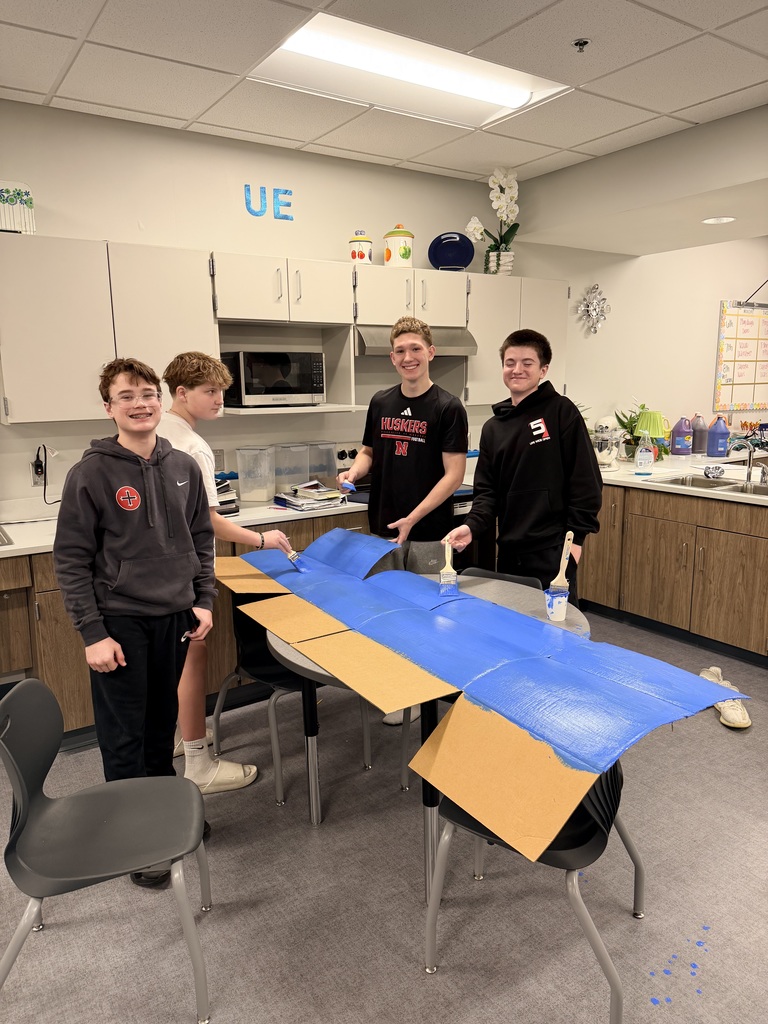 4 boys are painting cardboard and smiling at the camera. 