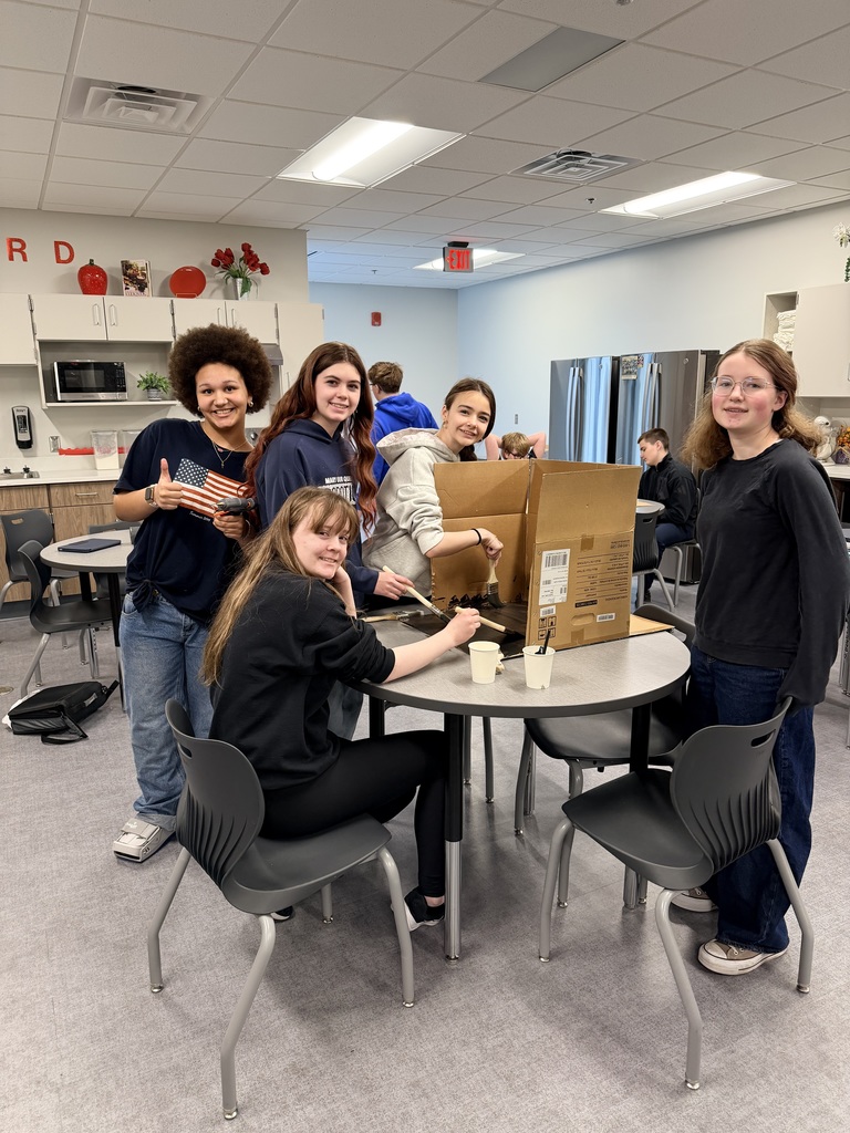 A group of girls sit around a table and smile at the camera. 
