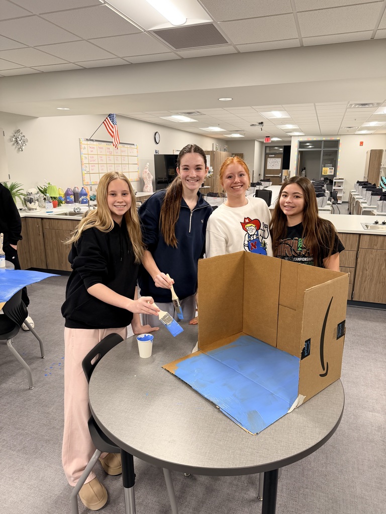 4 girls stand at their cardboard display and smile at the camera. 