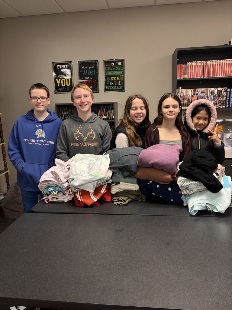 Photo of five students lined up behind a table with piles of sweatshirts in front of them.