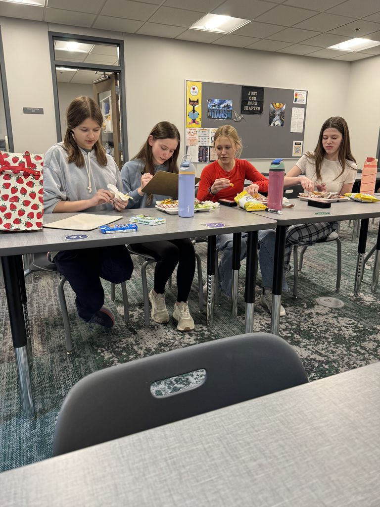 Four girls are eating lunch at a table and discussing. 