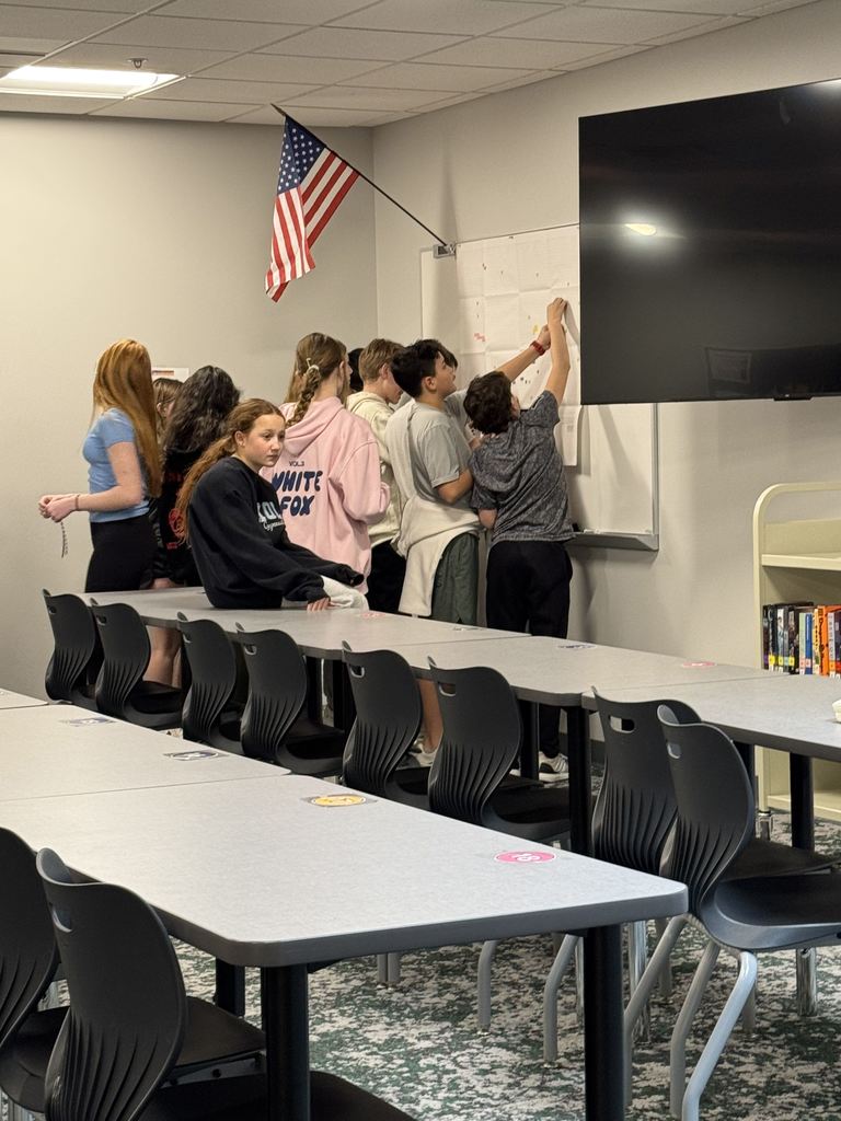 A group of students are putting stickers on a poster on a wall. 