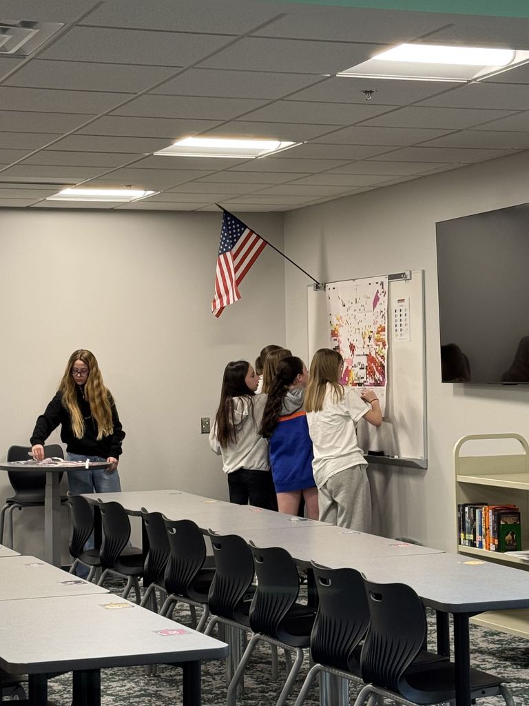 Girls are putting stickers on a poster on a wall. 