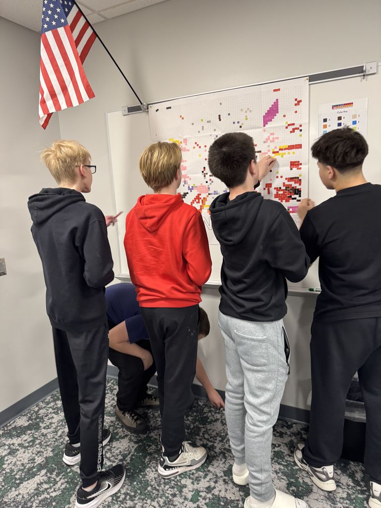 Boys are putting stickers on a poster on a wall. 