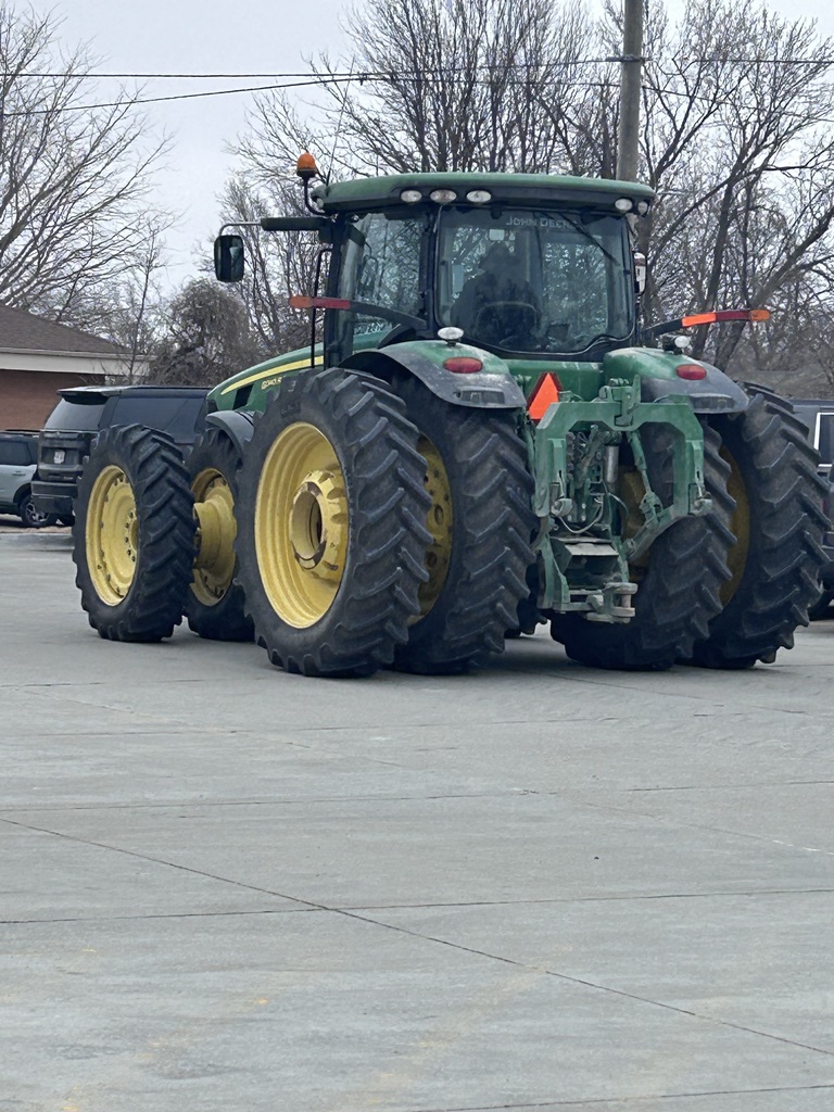 A rear view of a large green and yellow John Deere tractor parked on a concrete surface.
