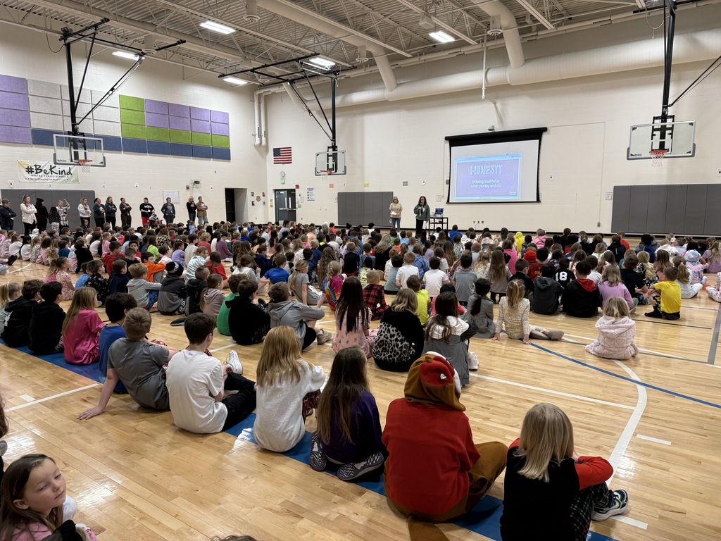 Students are sitting in the gym looking at a presentation reviewing honesty.
