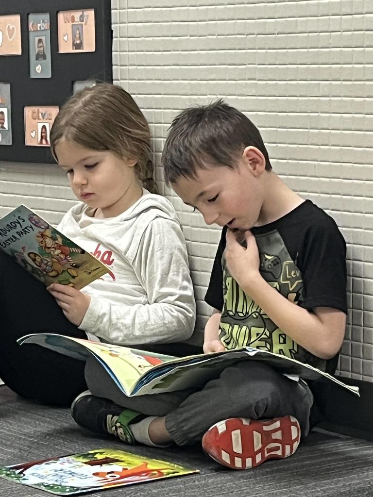 Two children sitting together against a wall; a girl reads a book titled "Corduroy's Easter Party" while the boy next to her looks at his own book with an expressive face.
