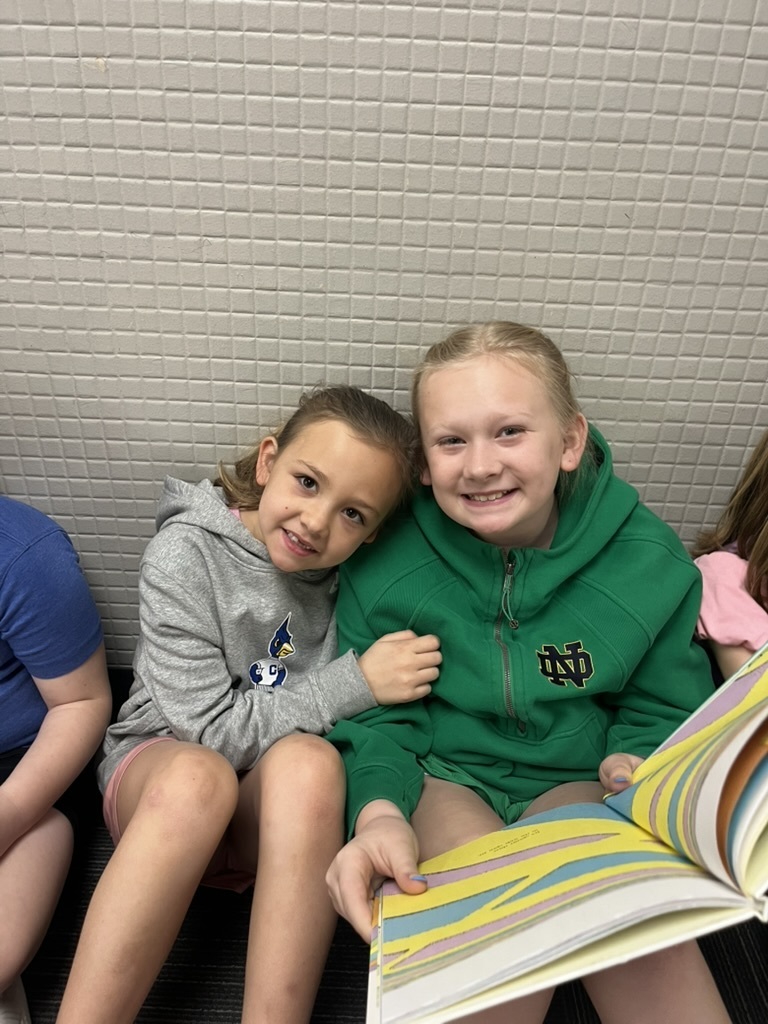 Two young girls sitting close together on the floor, smiling at the camera while holding an open Dr. Seuss book.