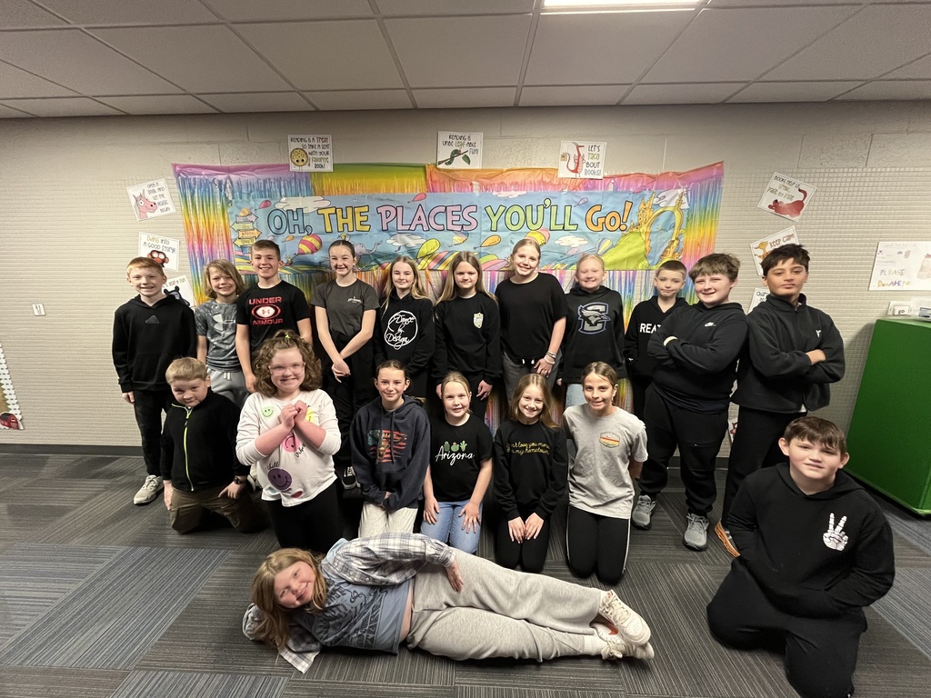 A large group of students posing together for a class photo in front of the colorful "Oh, The Places You'll Go!" wall display.