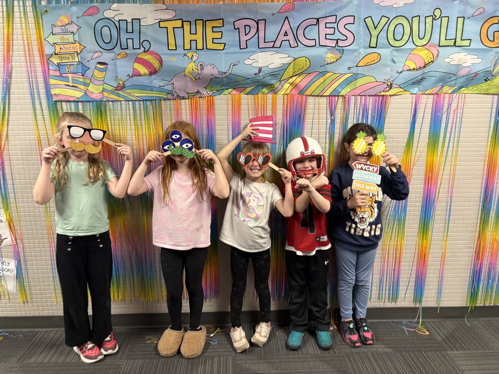 Five children stand in front of a colorful fringe backdrop holding up various paper eye-props and "Wacky Wednesday" signs.