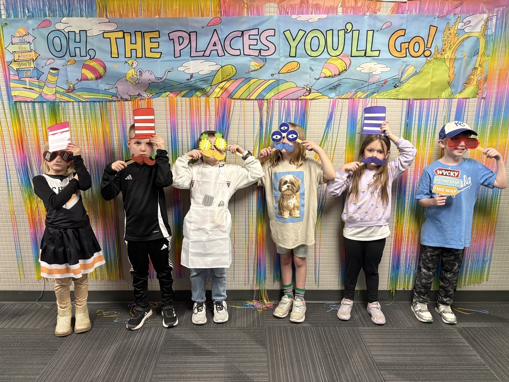 Six children stand in a line holding up colorful paper props (mustaches, hats, and glasses) in front of an "Oh, the Places You'll Go!" banner.