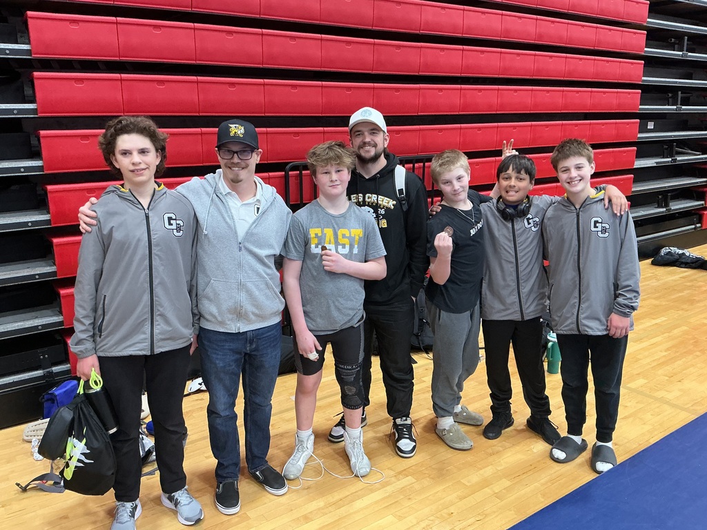 Five students and two coaches stand in front of bleaches smiling at the camera. 