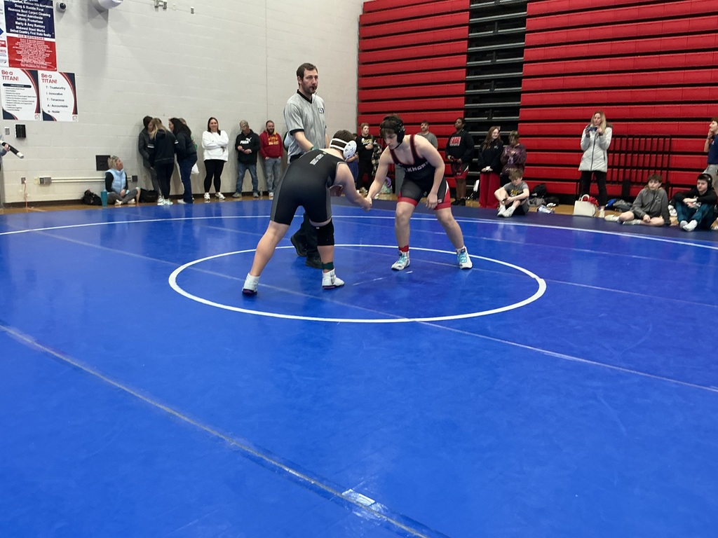 Two wrestlers shake hands in the middle of the mat. 