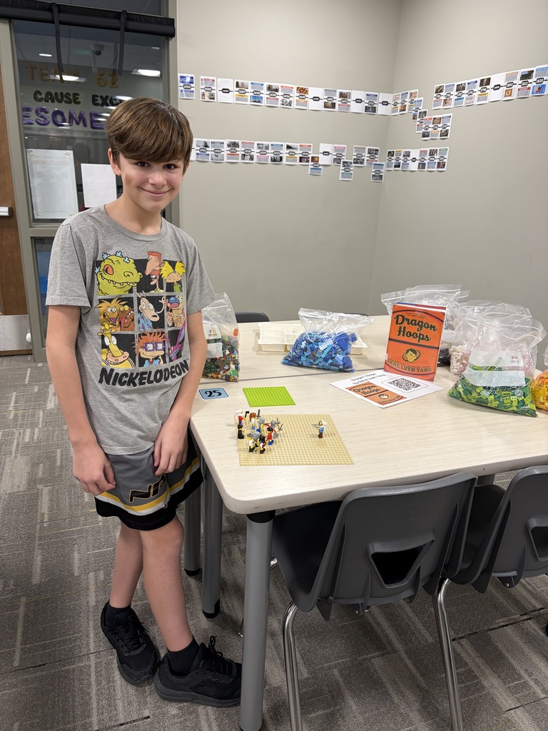 Photo of a male student standing next to a table showing off is Lego creation.