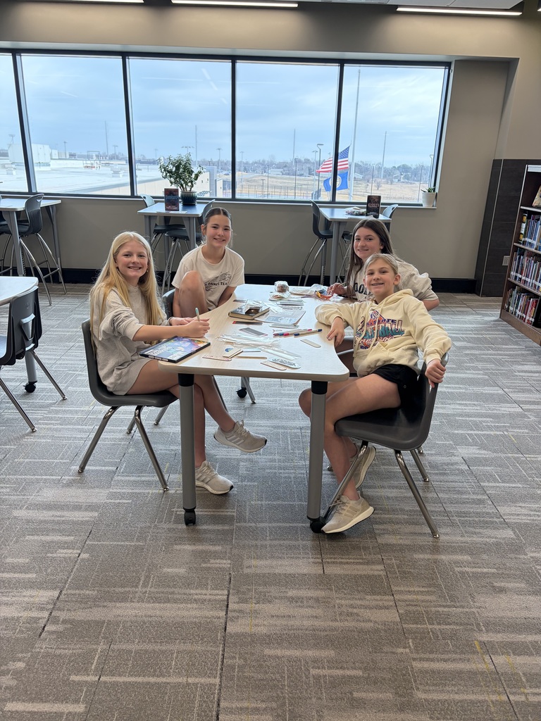 Photo of four female students sitting at a table coloring bookmarks.