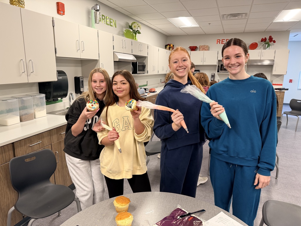 Four students are decorating cupcakes and smiling at the camera. 