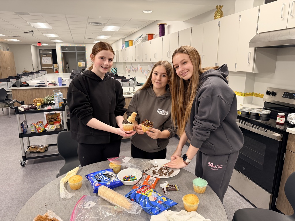 Three girls are decorating cupcakes and smiling at the camera. 