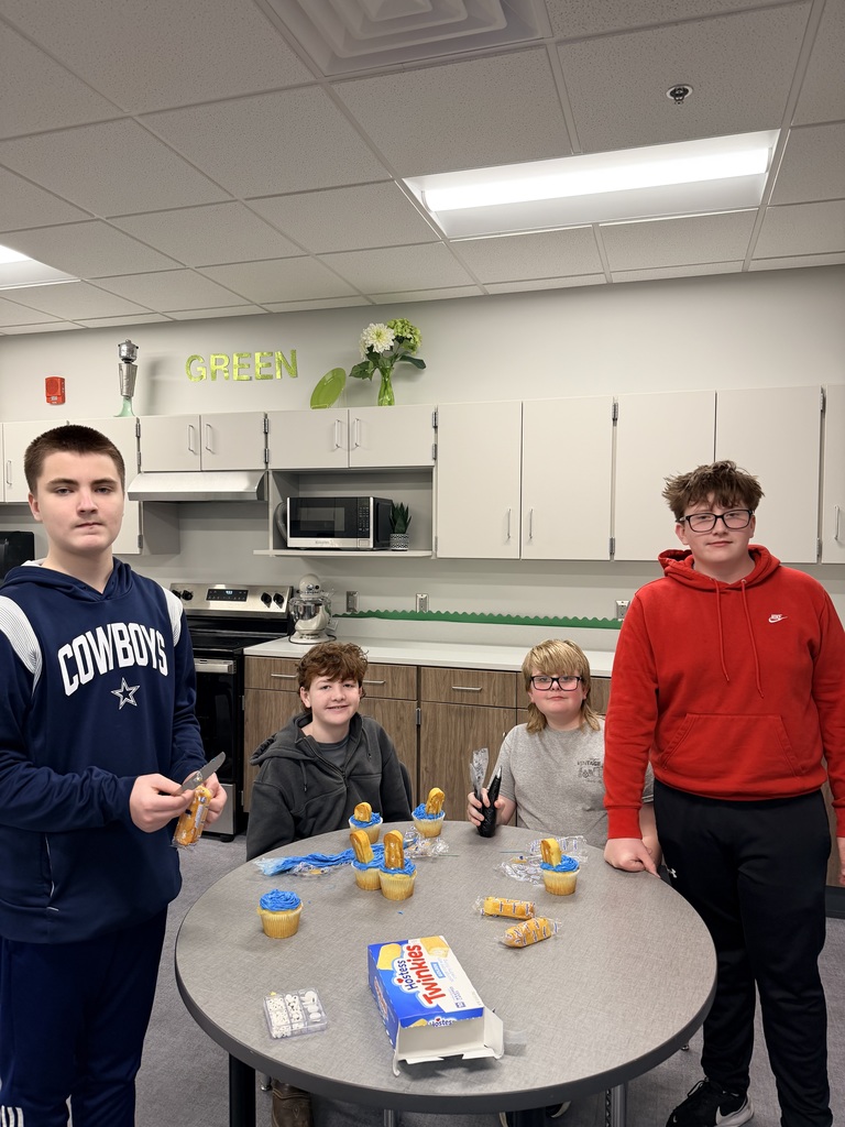 Four students are decorating cupcakes and smiling at the camera. 
