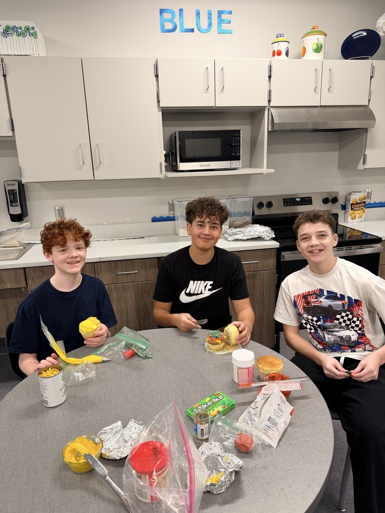 Three students are decorating cupcakes and smiling at the camera. 