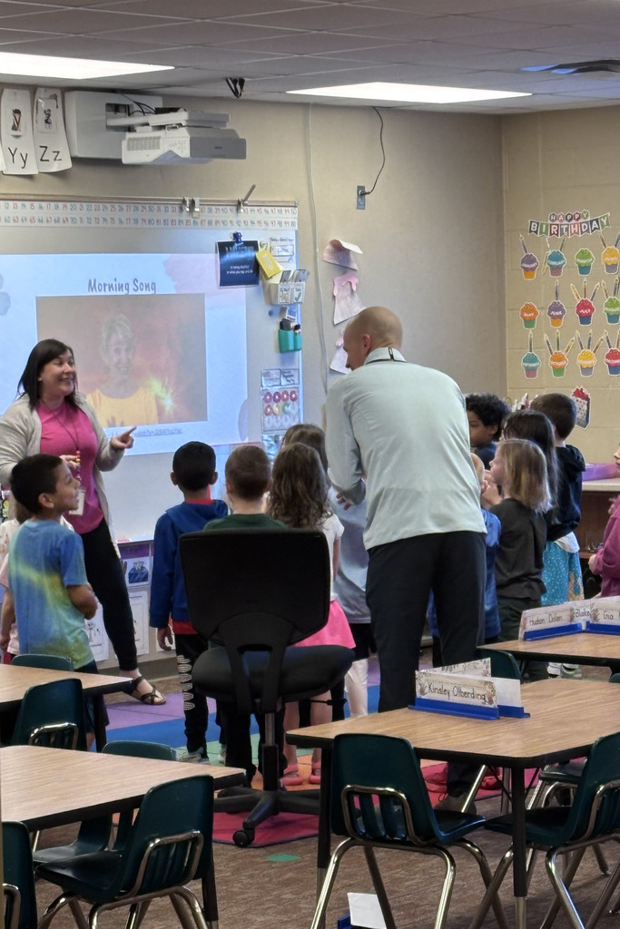 Board member Greg Beach presenting staff appreciation gift to teacher in classroom with students.