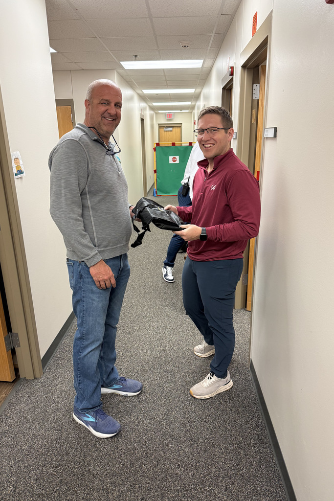 Board member Mark Hauptman  presenting staff appreciation gift to teacher in hallway.