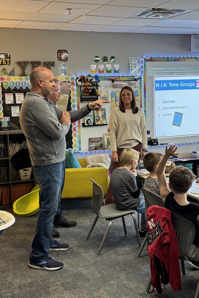 Board members Blake Turpen and Mark Hauptman presenting staff appreciation gift to teacher in classroom with students.