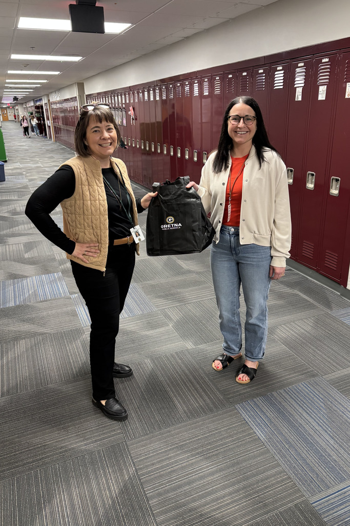 Board member Dawn Stock  presenting staff appreciation gift to teacher in school hallway.