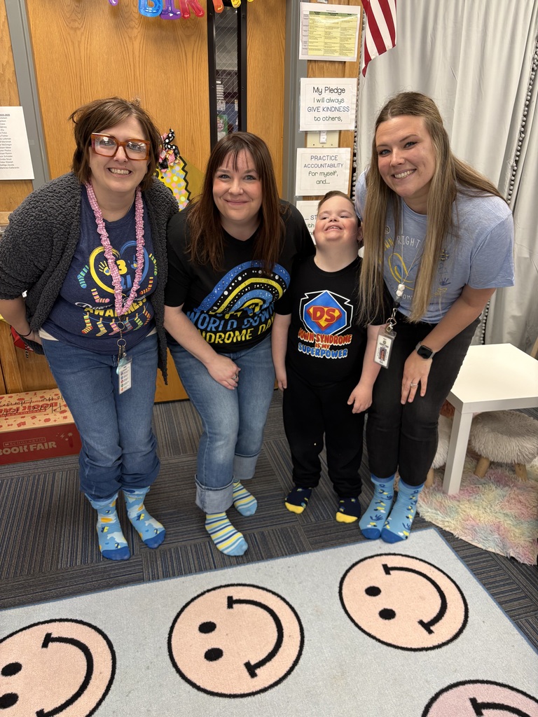 Three female teachers and a young boy standing together in the classroom, all wearing themed t-shirts and bright, mismatched socks.