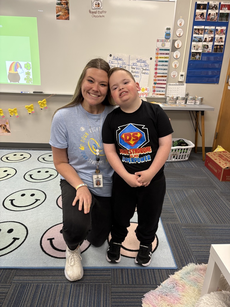 A heartwarming photo of a female teacher kneeling next to a young boy in a "Down Syndrome is my Superpower" shirt; both are smiling brightly.