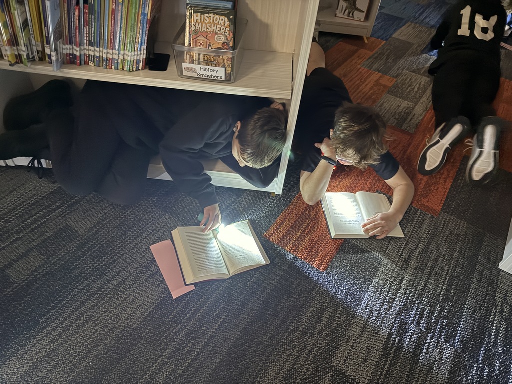 Two students are laying on the floor with flashlights reading.