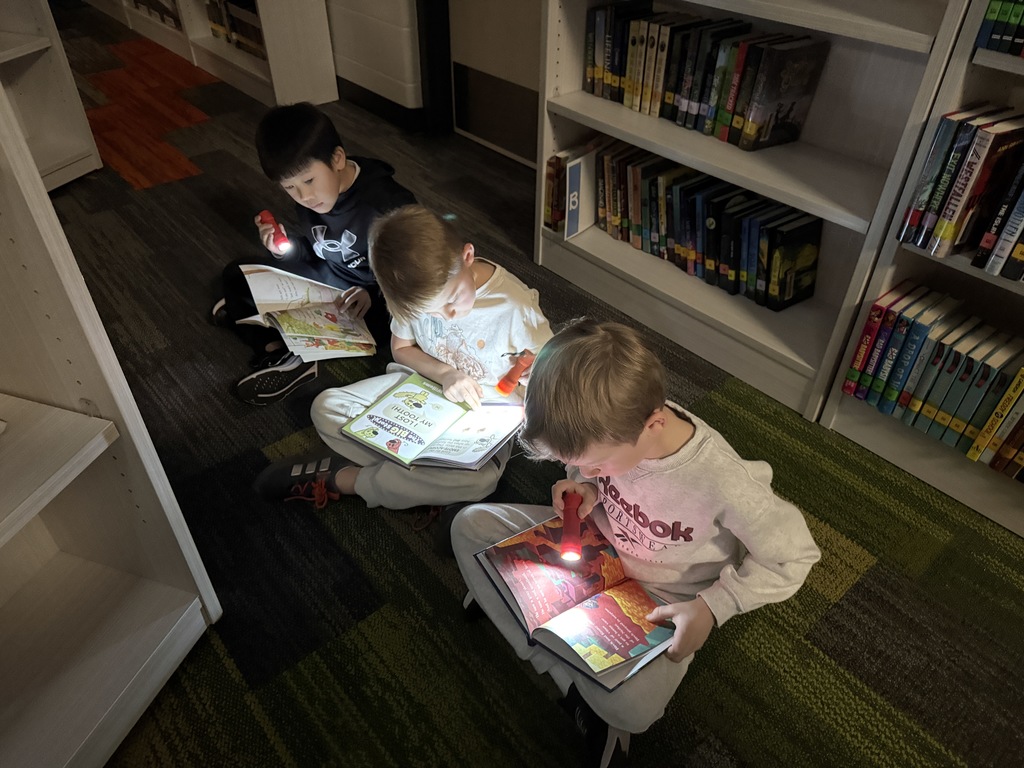 Three students are sitting on the floor with flashlights reading.