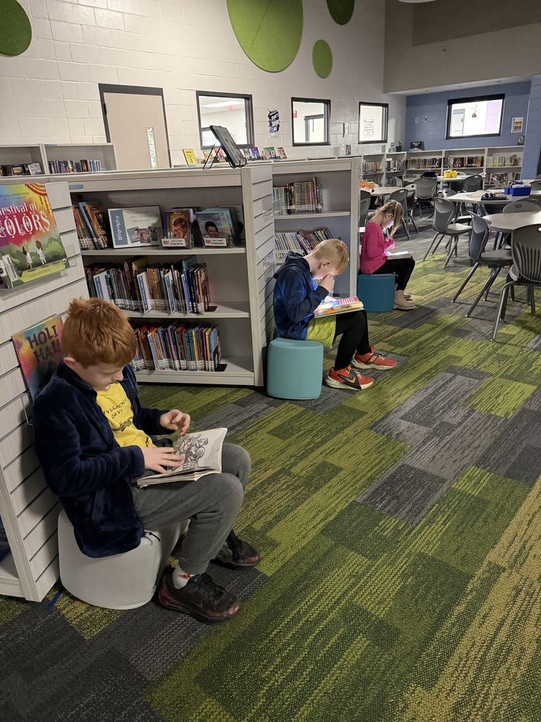 Three students are sitting on stools reading with flashlights.