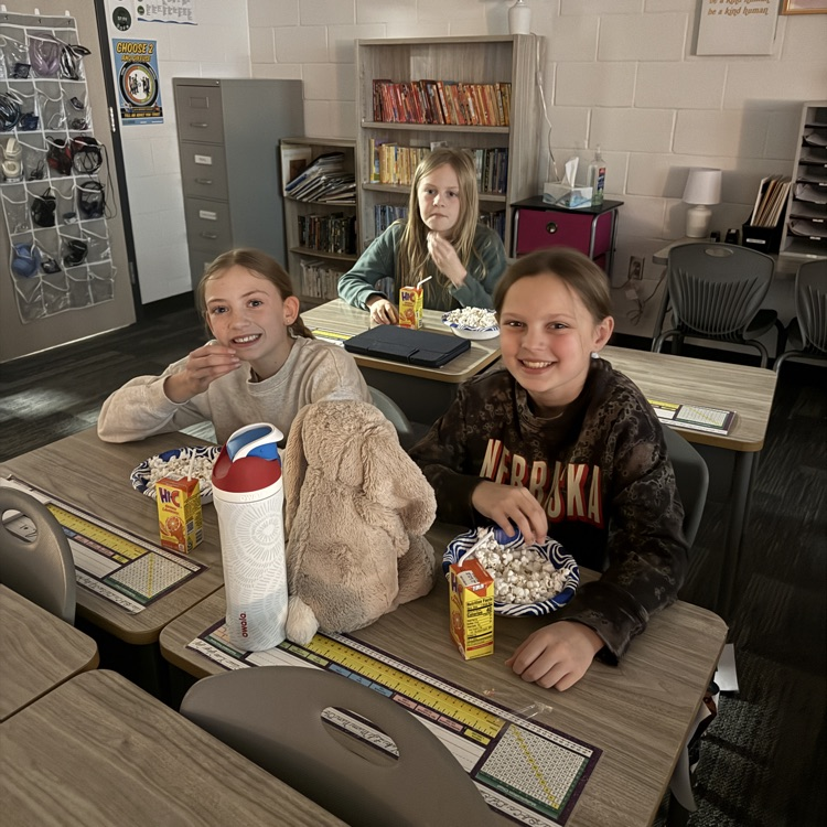 three girls eat popcorn at their desks  