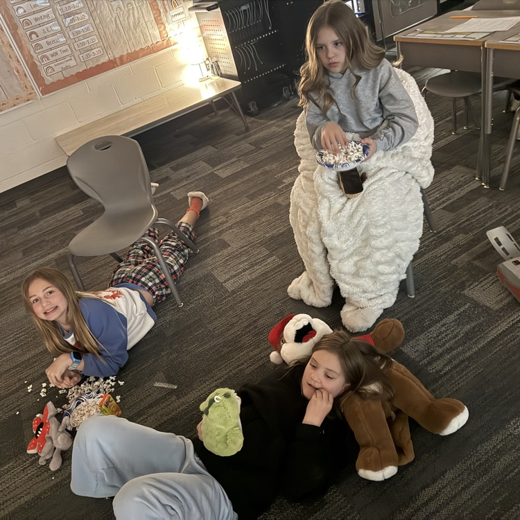 Three students are sitting or laying on the floor eating popcorn  