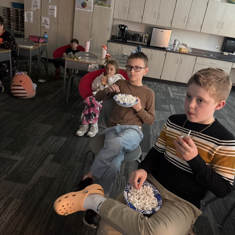 three students are sitting in their chairs eating popcorn 