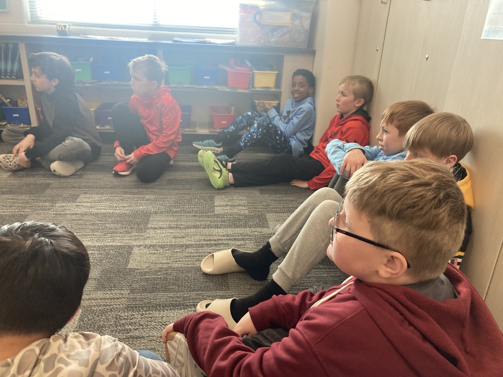 Students are sitting in a circle on the floor listening during a discussion around their persuasive writing.
