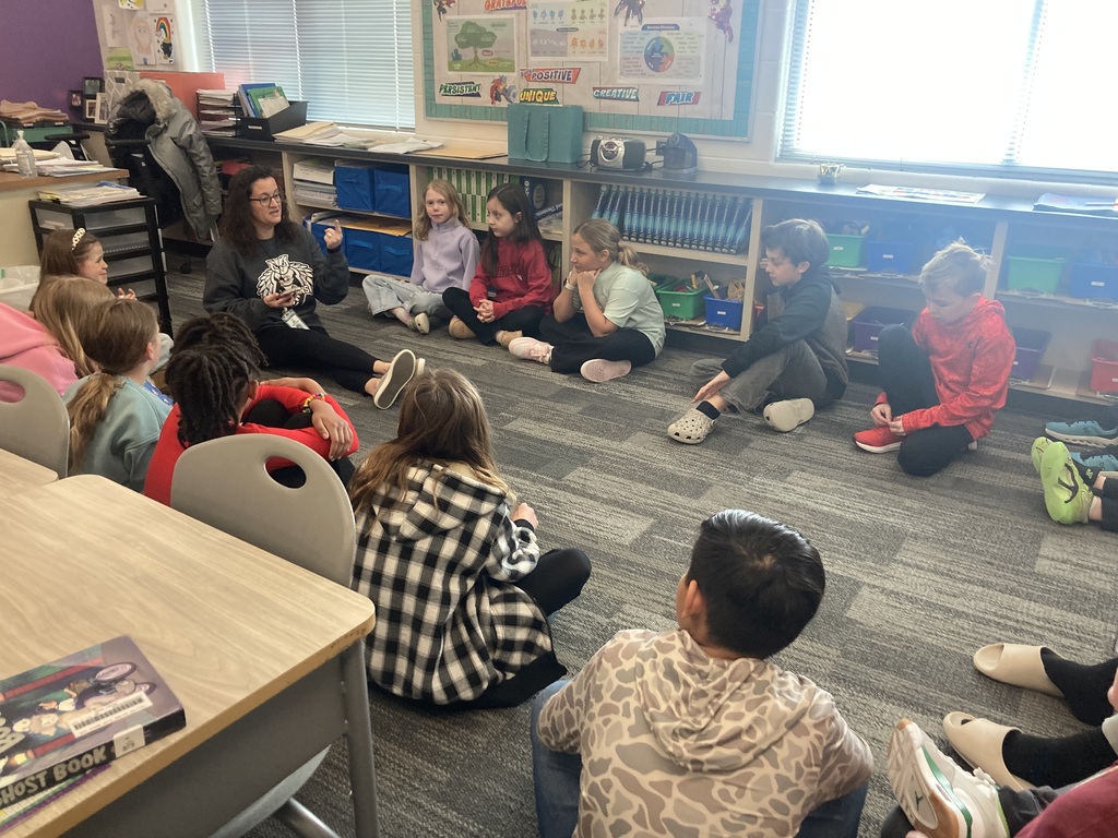 Mrs. Gabriel sits on the floor with students in a circle discussing their ideas brought up in their persuasive writing unit.