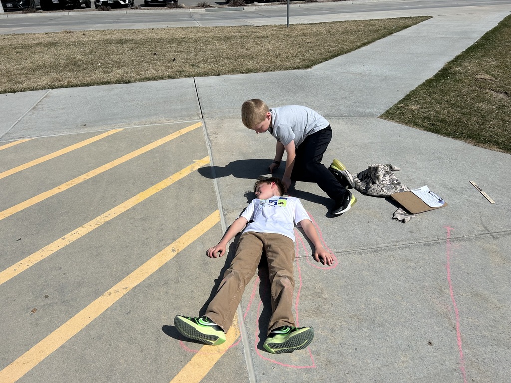students measuring and outlining one another with chalk