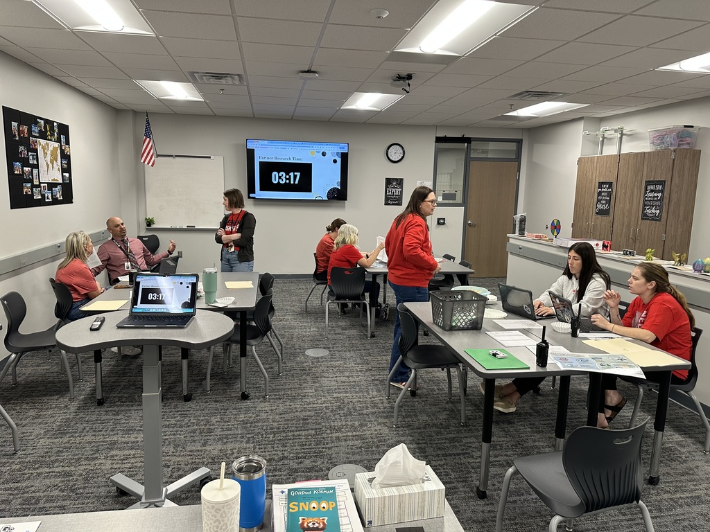 Teachers sit in groups in a classroom discussing items.