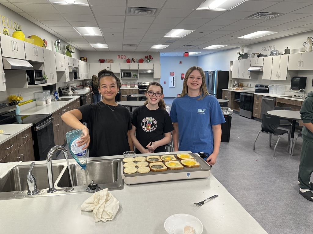 Three girls stand in front of a griddle and a sink, smiling at the camera.