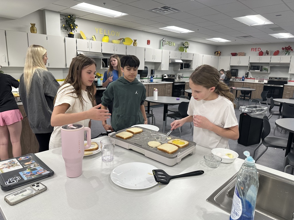 Students are making food at a griddle with others in the background.